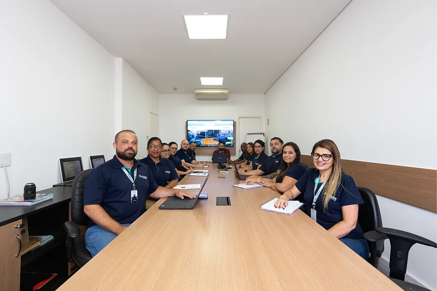 Colaboradores da Pizzani uniformizados reunidos ao redor de uma mesa em sala de reuniao da empresa.